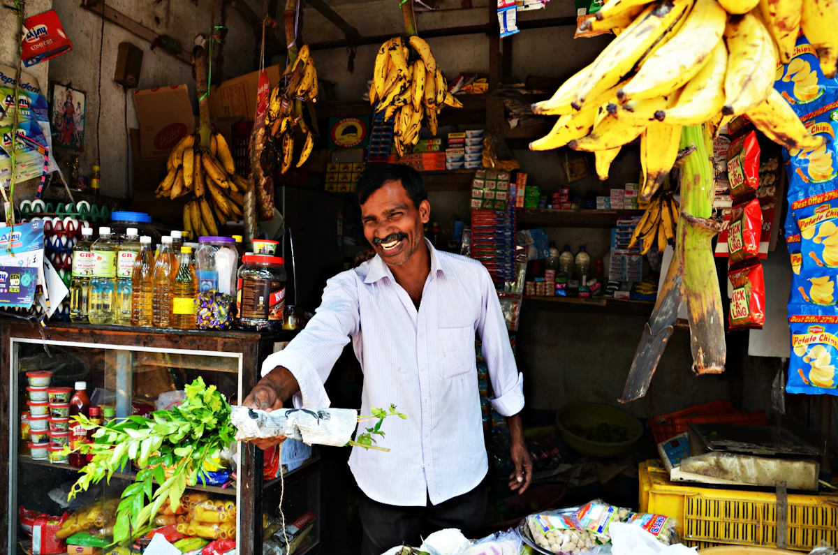 A shopkeeper smiling in front of his fruit and grocery stall